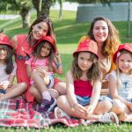 Friends enjoying a sunny day picnic on grass with bucket hats and smiles in a Portuguese park.